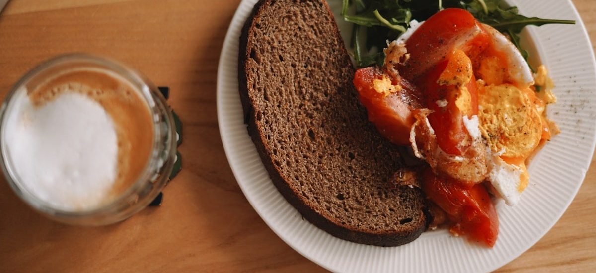 A cozy breakfast spread featuring rustic rye bread, bright tomatoes, and a perfectly poached egg, served with peppery arugula and a frothy latte