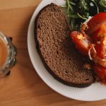 A cozy breakfast spread featuring rustic rye bread, bright tomatoes, and a perfectly poached egg, served with peppery arugula and a frothy latte