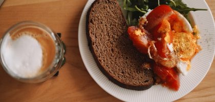 A cozy breakfast spread featuring rustic rye bread, bright tomatoes, and a perfectly poached egg, served with peppery arugula and a frothy latte