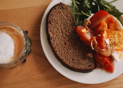 A cozy breakfast spread featuring rustic rye bread, bright tomatoes, and a perfectly poached egg, served with peppery arugula and a frothy latte