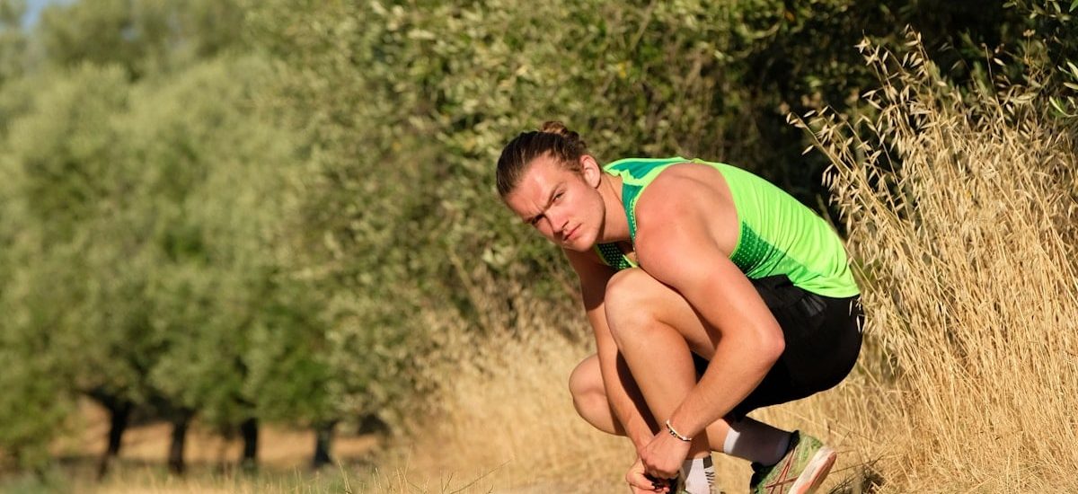 a man squatting down in a field with trees in the background