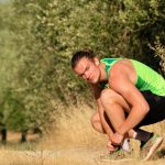 a man squatting down in a field with trees in the background